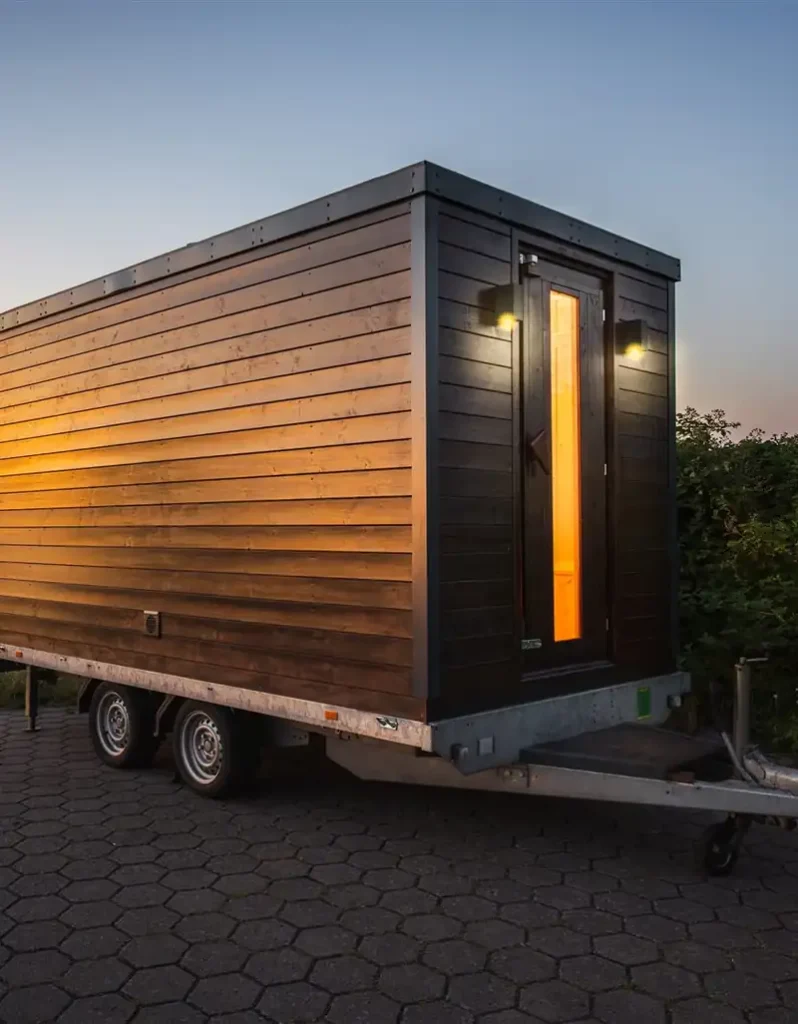 Mobile Sauna auf Anhänger mit beleuchteter Glastür am Abend