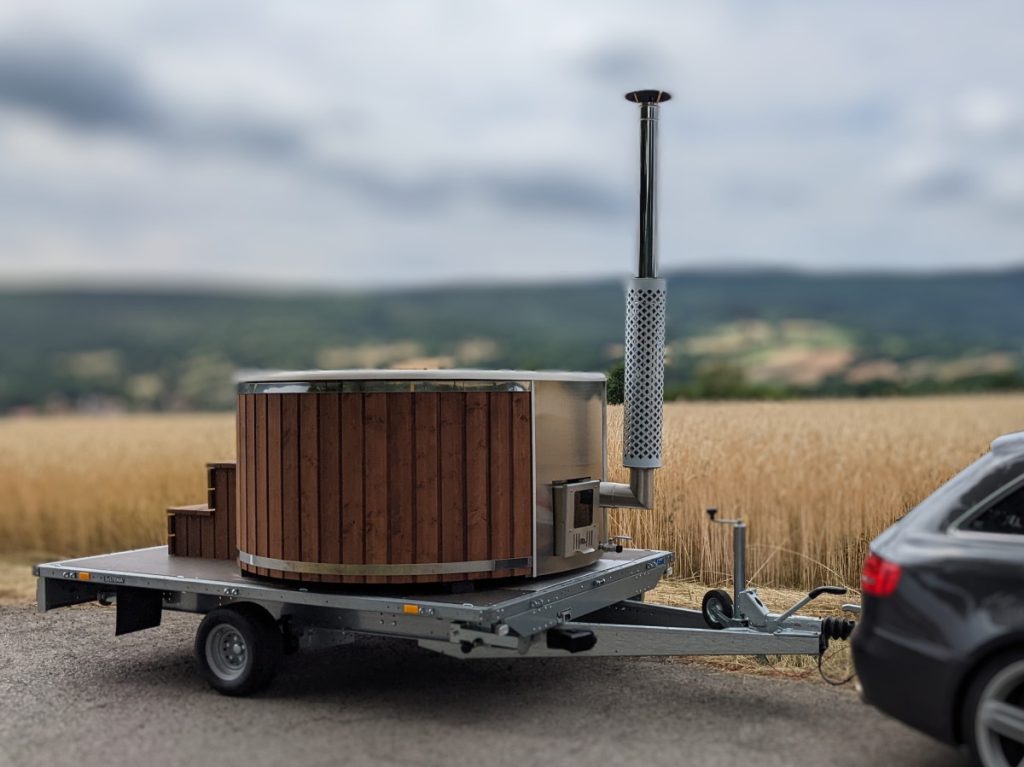 Mobiler Whirlpool mit Holzofen auf Anhänger vor einem Kornfeld