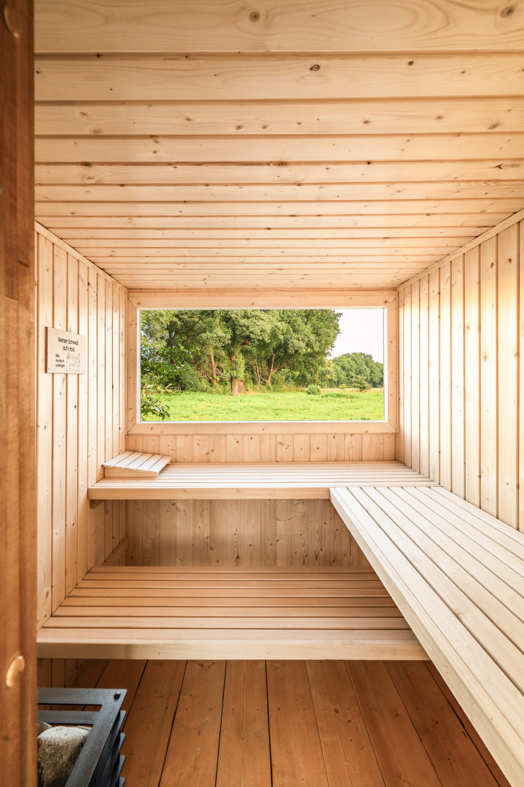 Helle Saunakabine aus Holz mit Panoramafenster und L-förmigen Saunabänken
